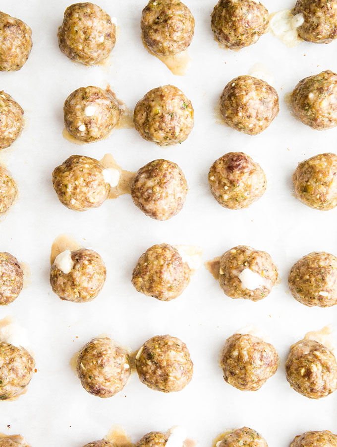 The meatballs are baked on a parchment paper lined baking sheet for 20 minutes.