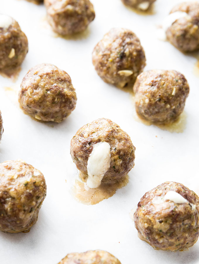 The cheese stuffed meatballs are baked on a parchment paper lined baking sheet.