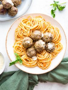 Mozzarella stuffed meatballs are plated in a bowl next to a napkin and fresh basil.