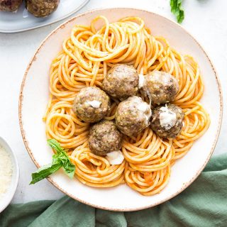 Mozzarella stuffed meatballs are plated in a bowl next to a napkin and fresh basil.
