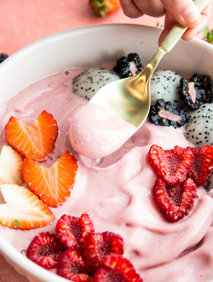 A spoonful of smoothie bowl is lifted by the spoon over a white bowl.