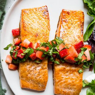 Salmon fillets are topped with fresh strawberry relish and plated next to a salad.
