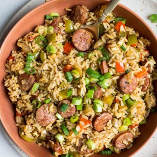 Cajun rice is plated in a red bowl and stirred with a gold spoon and topped with green onions.