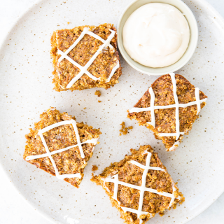 Carrot cake oatmeal bars are sliced and plated on a plate next to a bowl of the icing.