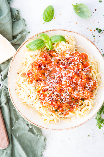 Pasta is plated in a bowl and topped with pomodoro sauce and cheese.
