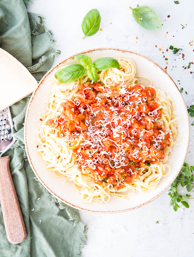 Pasta is plated in a bowl and topped with pomodoro sauce and cheese.