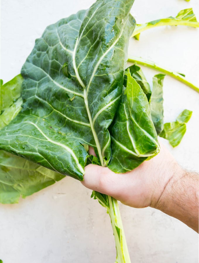 A hand is ripping the collard leaf from the stem