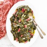 Collard greens and smoked turkey necks are plated on a white plate with two utensils.
