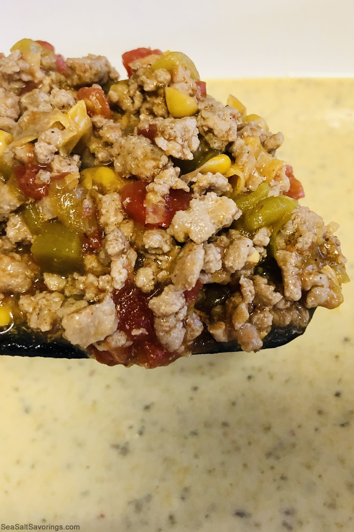 a spoon full of filling hovering over a baking pan that has cornbread batter in the bottom