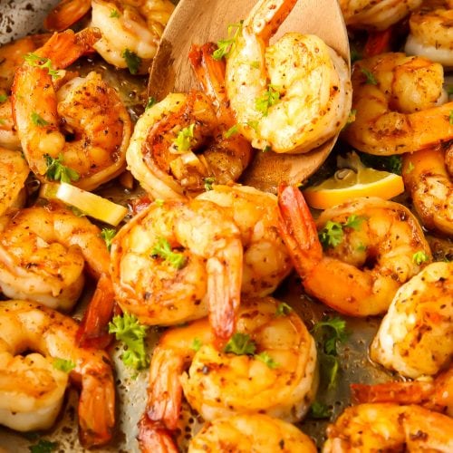 A spoon is lifting shrimp out of the pan it was cooked in.