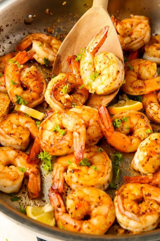 A spoon is lifting shrimp out of the pan it was cooked in.