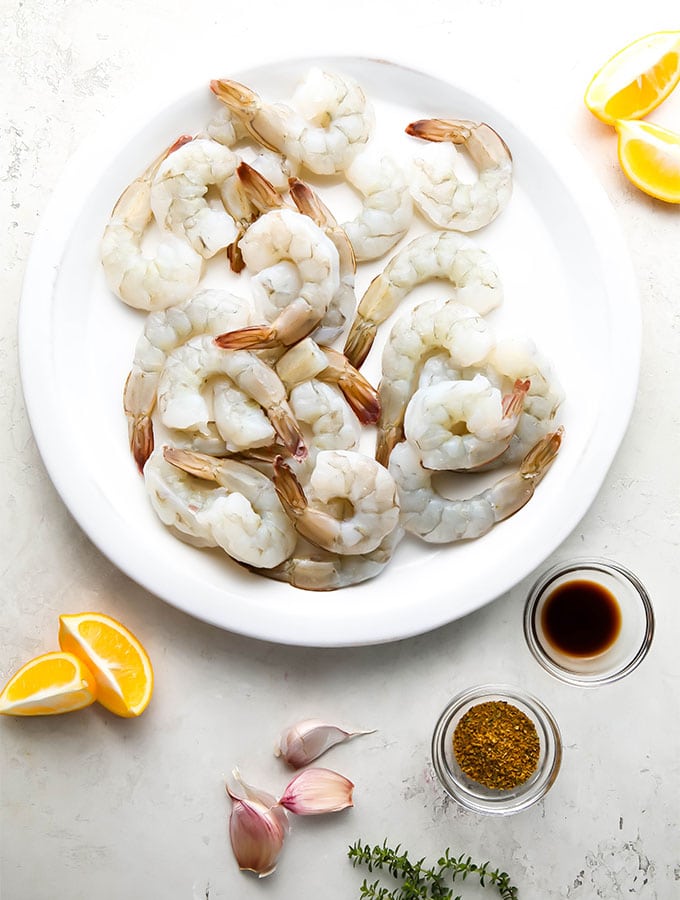 Shrimp, lemons, spices, thyme, and worcestershire sauce is placed on a table.