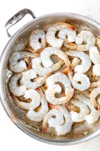 Shrimp is placed in a pan to sear them quickly with butter and spices.