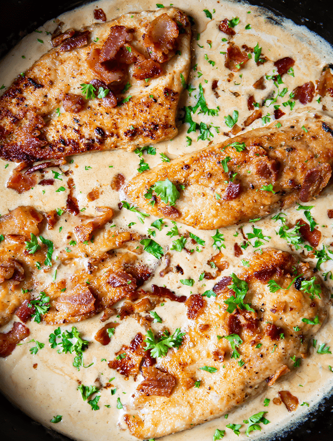 chicken breasts in frying pan simmering in sauce