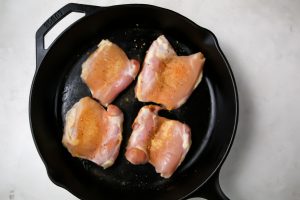 Chicken thighs are placed in the cast iron pan and seasoned.