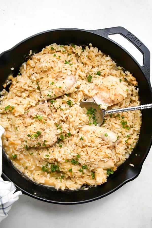 Chicken and rice casserole is cooked in a cast iron skillet and topped with fresh parsley.