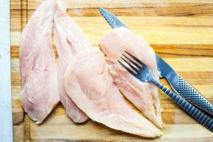 Chicken breasts are halved with a shark knife and a fork before they are seasoned.