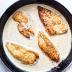 Pan seared chicken is added to the cream sauce in a cast iron pan.
