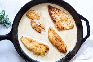 Pan seared chicken is added to the cream sauce in a cast iron pan.
