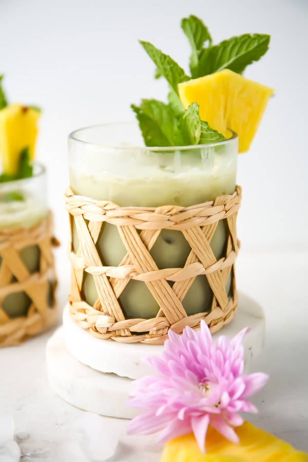 Pineapple matcha drink is poured into a small glass and garnished with mint and fresh pineapple.