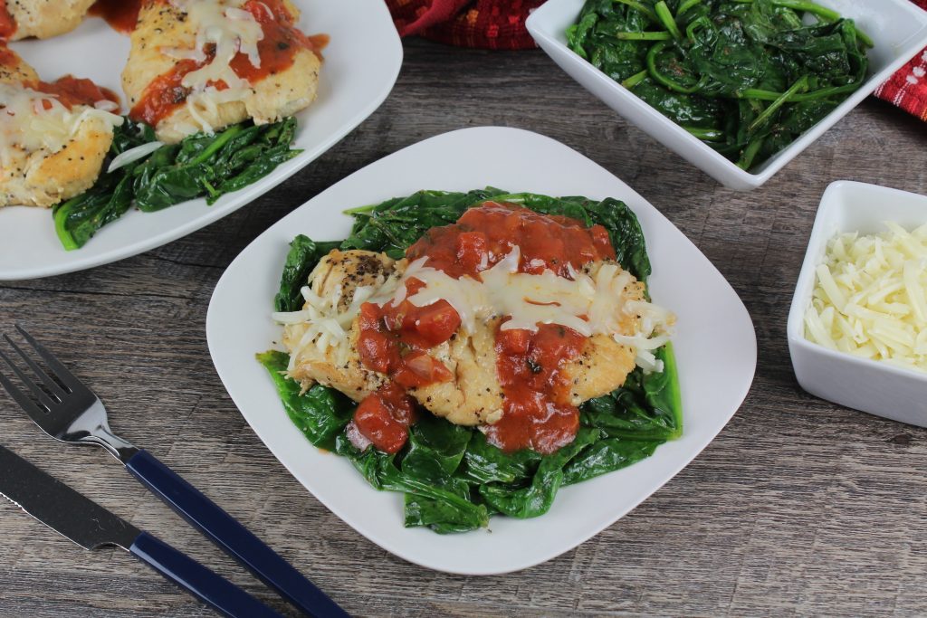 plate of chicken with red sauce drizzled on top as it lays on a bed of cooked spinach