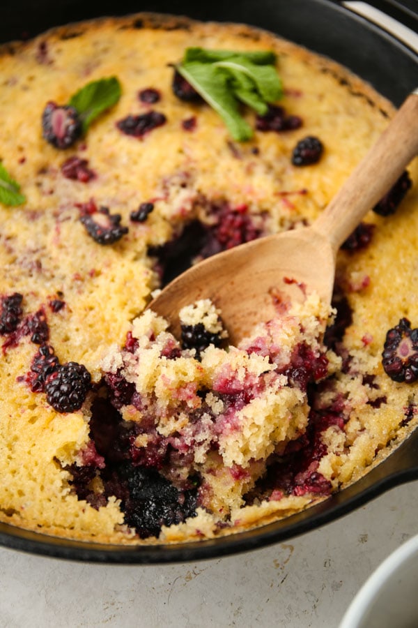 A spoon is serving a heaping of blackberry cobbler.