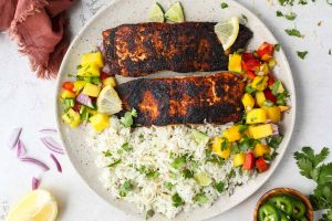 Blackened salmon is plated on a plate with coconut rice, and mango salsa.
