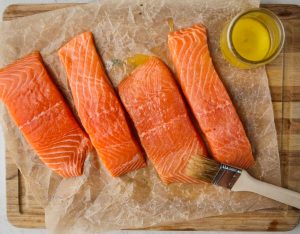 A brush slathers the salmon in melted butter ontop of parchment paper.