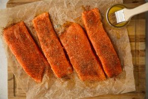 Salmon filets are plated on parchment paper and brushed with butter and blackening seasoning.