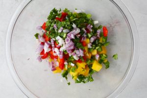 Mango salsa is made with red onion, cilantro, mango, and red pepper.