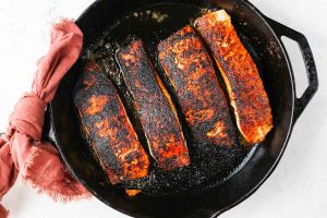 Salmon is pan seared in a hot cast iron until it is blackened.