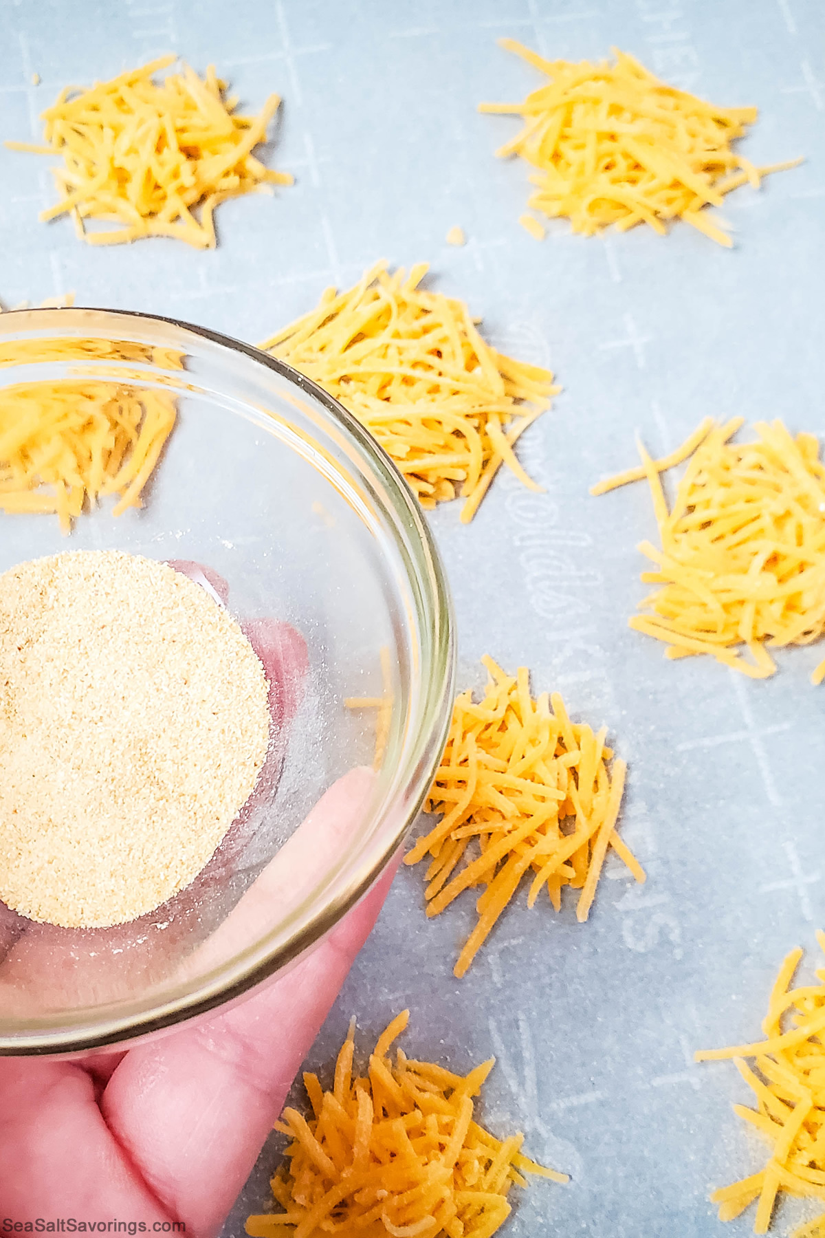 sprinkling garlic powder on top of little mounds of cheese on a baking sheet