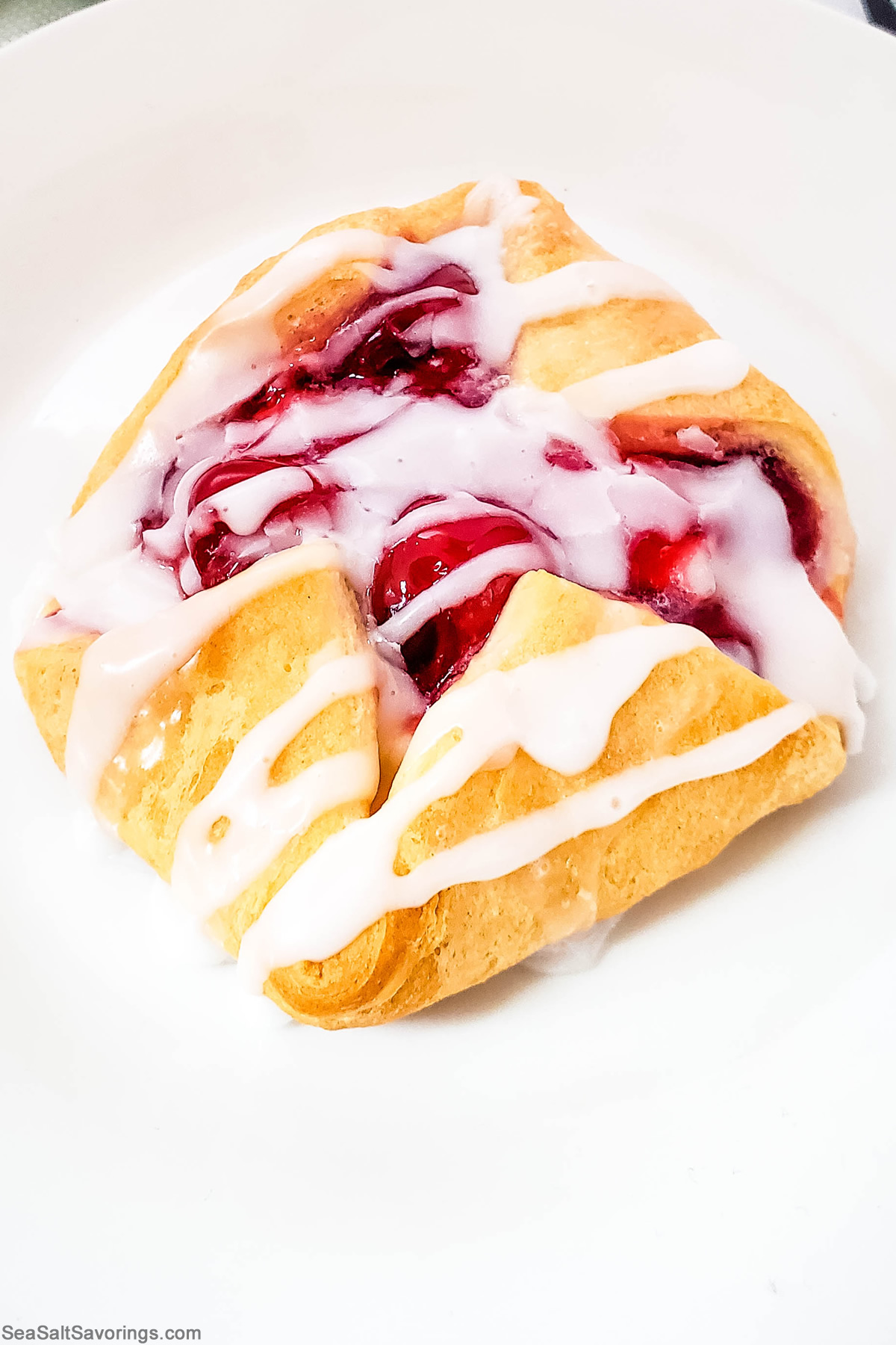 close up view of a cherry cheese danish drizzled with frosting