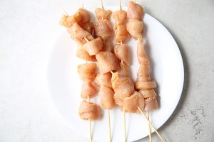 Chicken is strung on wooden kabob sticks before they are grilled.