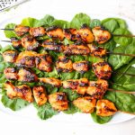 Grilled chicken kabobs are plated on a bed of spinach on a white plate.