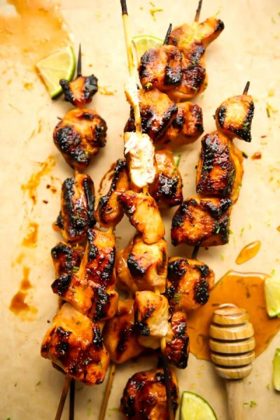 Grilled chicken kabobs are plated on parchment paper and a piece of chicken it bitten into.