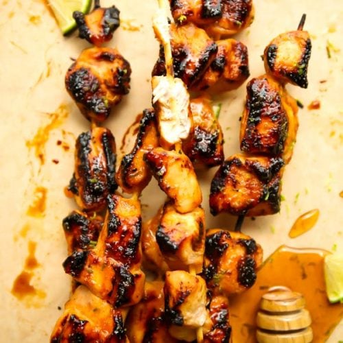 Grilled chicken kabobs are plated on parchment paper and a piece of chicken it bitten into.