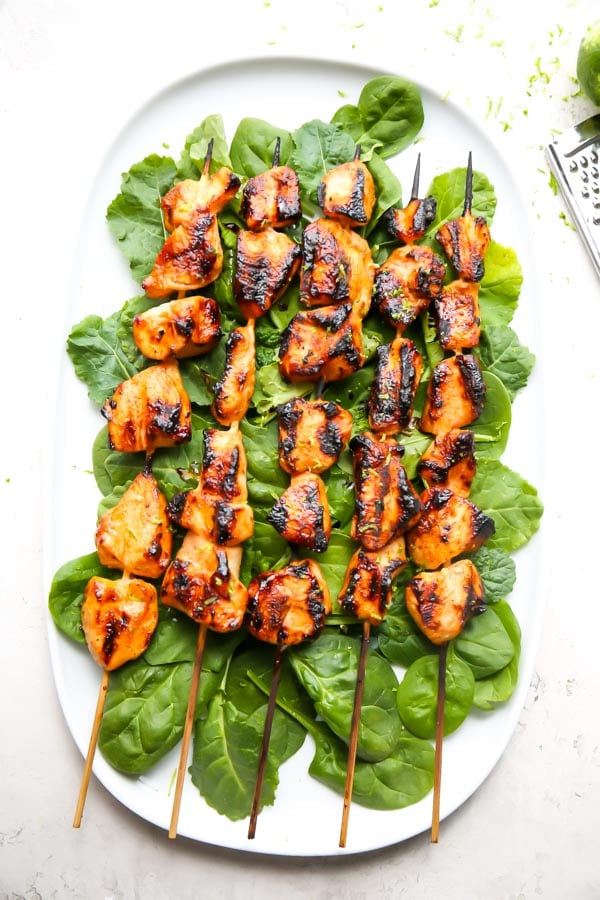 Grilled chicken kabobs are plated on a bed of spinach on a white plate.