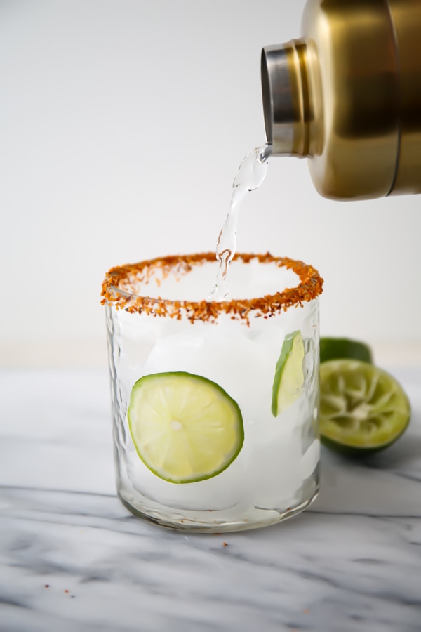 salt rimmed glass with lime slicers pouring drink mixture