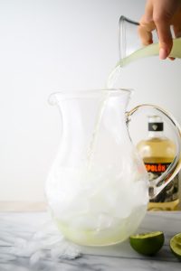 Lime juice is poured into the glass pitcher on top of ice.