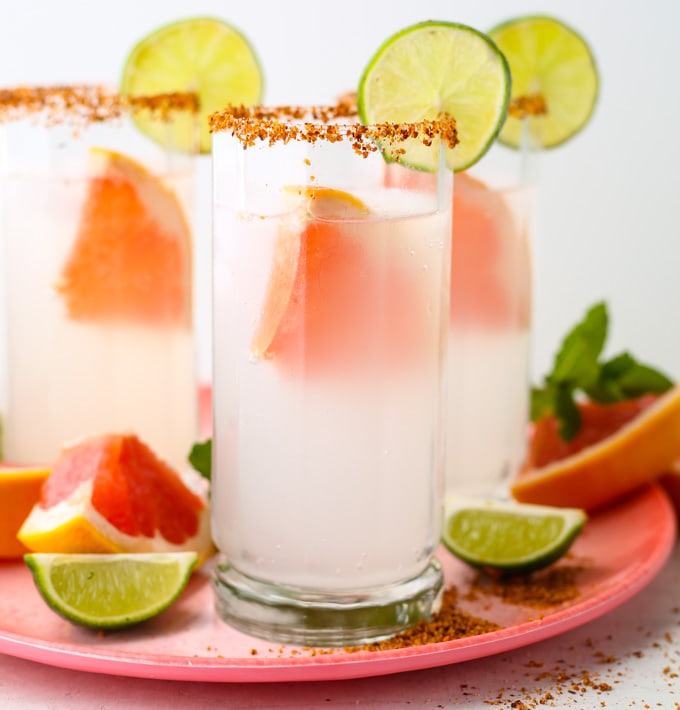 glass filled with paloma cocktail mix on a plate with fresh cut slices of lime