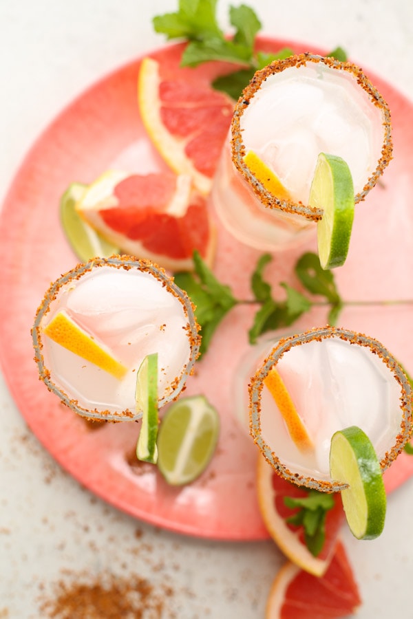 Palomas are plated on a pink plate with grapefruit and lime wedges.