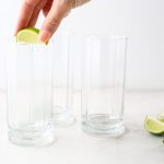 A hand is rubbing a lime wedge around the rim of the glass.
