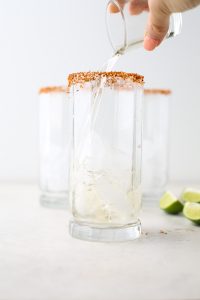 A hand is pouring tequila into a glass full of ice.