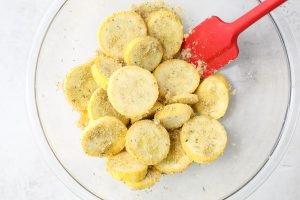 The sliced summer squash is tossed with the breadcrumbs, seasoning, and oil in a large bowl.