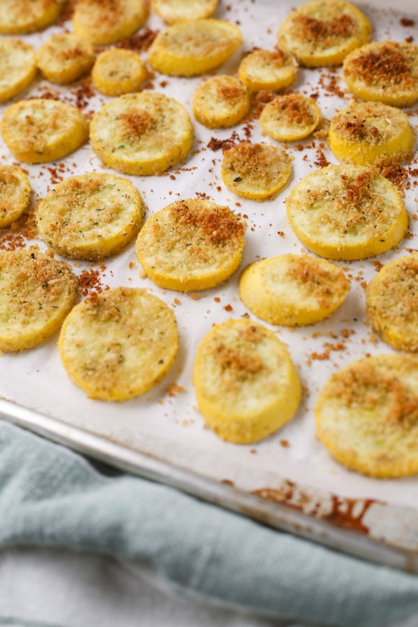 The summer squash is roasted on a parchment paper lined baking sheet until it is golden brown.