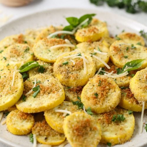 Sliced roasted summer squash is placed on a white plate and topped with parmesan cheese.