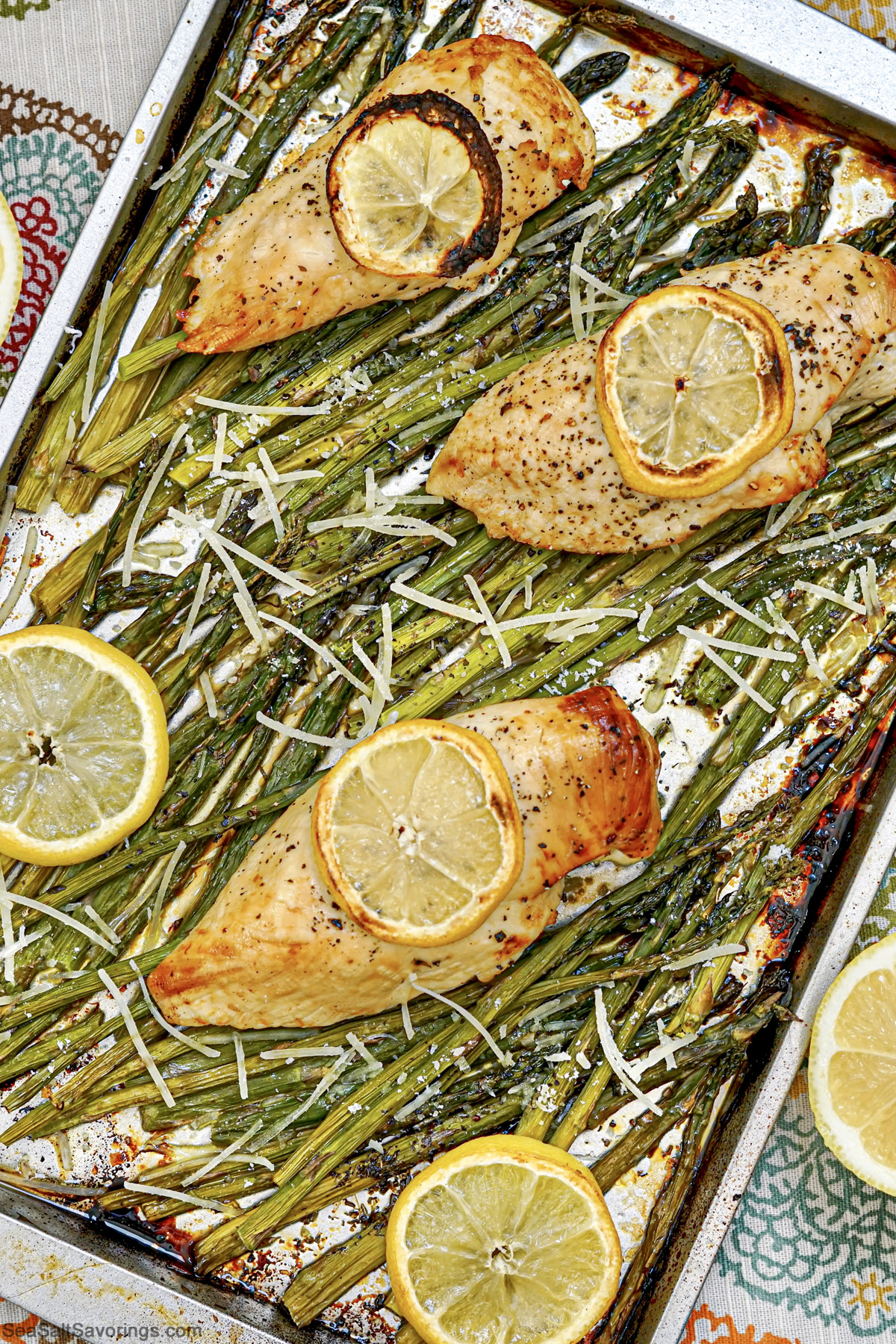 sheet pan with baked chicken and asparagus on it and lemon garnish