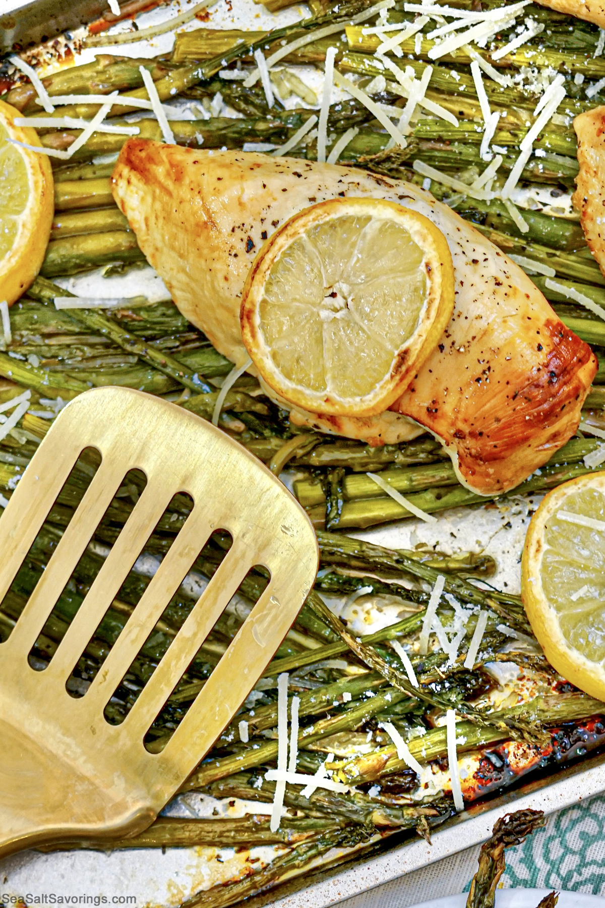 sheet pan with baked chicken and asparagus on it and lemon garnish