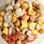 The shrimp, crawfish, corn, potatoes, butter, and seasoning are tossed together in a bowl to evenly coat everything.